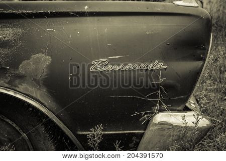 Croswell, Michigan, USA - August 24, 2017: Rusted front fender and logo of a 1966 Plymouth Barracuda rusting in a field.