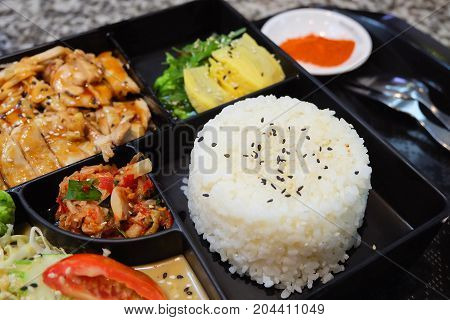 Traditional Japan Cuisine Bento Box or Multi-Layered Box with Teriyaki Chicken Rice Salad Tamagoyaki or Rolled Omelette Hiyashi Wakame or Seaweed Salad and Kimchi Served with Paprika Powder.