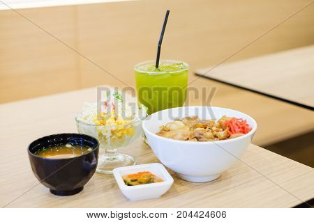 The food set consists of rice with grilled pork teriyaki spring onion & carrot on top white bowl serve with tofu soup (Miso soup) tomato cabbage & corn salad and green tea - japanese food concept.