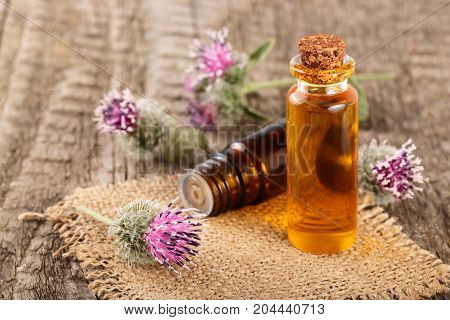 burdock oil in glass bottle and burdock flowers on an old wooden background.
