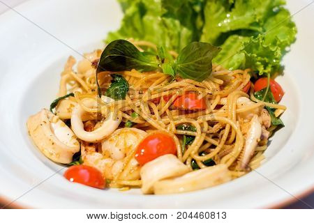 The spaghetti spicy seafood (squid shrimp) with basil tomato black pepper lettuce and paprika on white dish set on table for food background or texture - homemade food concept.