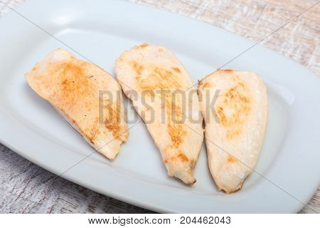 Slices of roasted chicken breast and tomato on white plate.
