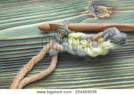 Warm green winter yarn ball for knitting and crochet on the wooden table. Closeup crochet chain photo. Rustic crochet thread and a bamboo hook. Rustic background for creative craft work. Work place