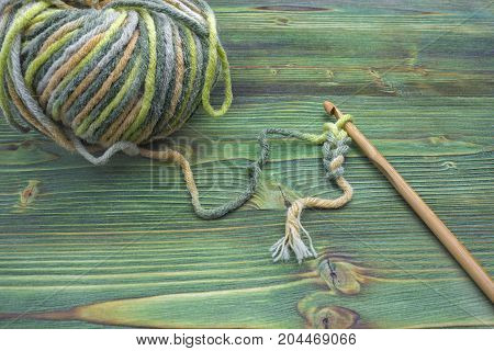 Rustic crochet thread and a bamboo hook. Warm green winter yarn ball for knitting and crochet on the wooden table. Rustic background for creative craft work. Work place top view