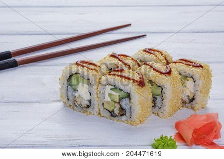 Set of eight rolls with eel sesame avocado and philadelphia cheese decorated with wasabi and ginger on a wooden white background Sushi and chopsticks