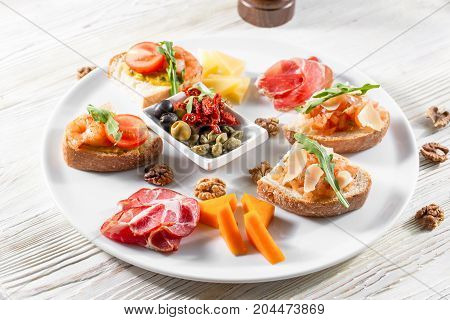 Selection of tasty bruschetta or canapes on taosted baguette and quark cheese topped with smoked salmon, shrimp, prawn, olives, tomato and chorizo sausage