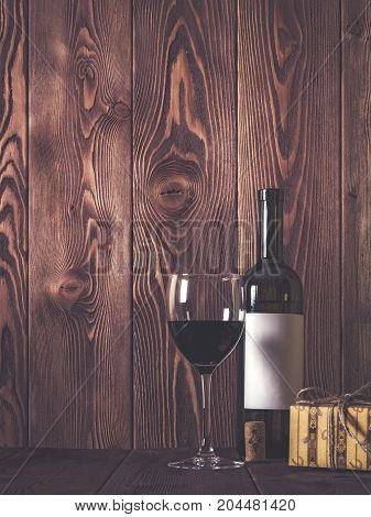 Bottle of wine wineglass and gift box on wooden table. Retro style. Dark toned