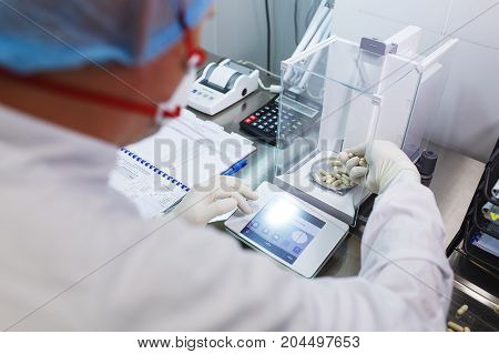Pharmacist, a laboratory worker in sterile rubber gloves, weighs the manufactured tablets on the control scales.