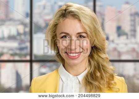 Detail of smiling young woman. Close up portrait of attractive blod girl smiling on office widow background.