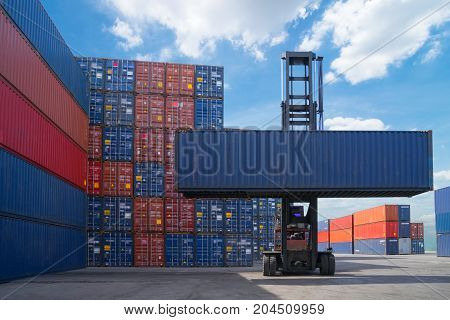 Forklift truck lifting cargo container in shipping yard or dock yard against sunrise sky with cargo container stack in background for transportation import, Export and logistic industrial concept