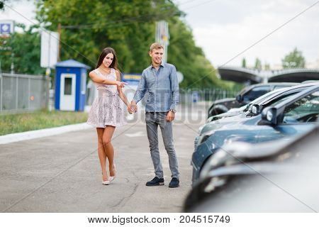 A young guy with a girl walks in the parking lot and chooses a car.