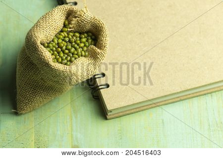 Mung bean on sack with brown book on wooden of green pastal color
