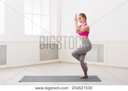 Fitness, woman training yoga in eagle pose in gym at white background, copy space. Young slim girl makes exercise.