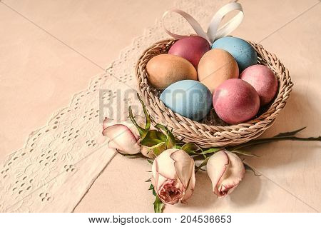 Dyed eggs with rose buds and satin bow in a wattled basket on white lace border