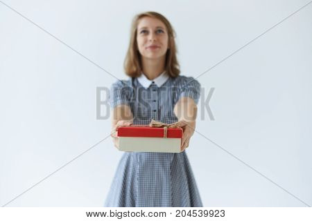 Elegant young Europen lady in collar dress holding big box of present giving it to her friend on birthday. Attractive girl making gift posing at studio wall. Selective focus on female's hands