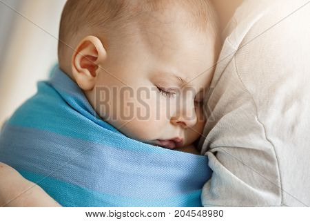 Close up of innocent little child, sleeping on mother hands in blue baby slim. Quite and relaxing scene.