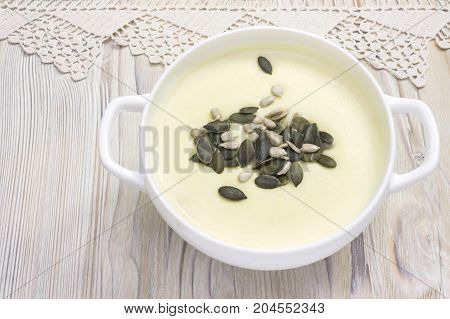 Potato and onion vegan vegetarian healthy cream soup with pumpkin and sunflower seeds white bowl. Tasty potato soup and handmade crochet napkin on rustic wooden table. Traditional lunch or dinner