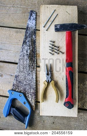 Saw - hacksaw pliers screws hammer nails - on a bar and wooden unplaned boards. Hand tools for building a frame house.