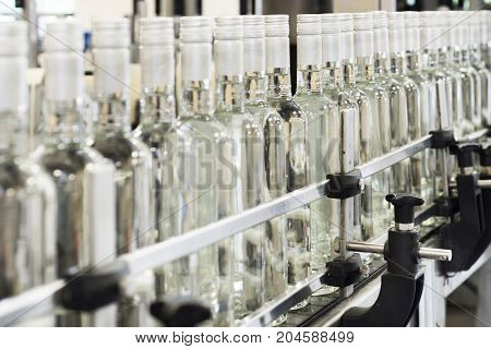 A long row of glass bottles on the conveyor. The bottles are closed with a screw cap.
