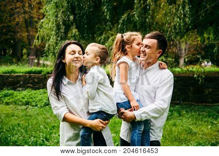 family of four people portrait in city park kids kissing perents