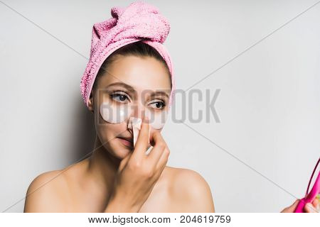 Young beautiful woman with a mask under the eyes looks at herself in the mirror, cleanses the skin