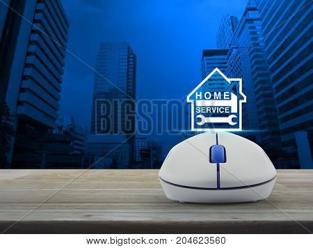Hammer and wrench and house icon with wireless computer mouse on wooden table over modern office city tower Home service concept