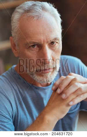 Morose glance. Close up of a serious aged man holding his hands in a lock while expressing confidence