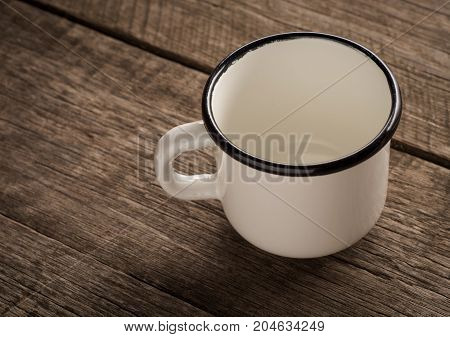Old enamel empty cup on a wooden surface.