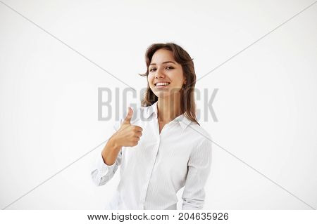 Successful young Latin businesswoman wearing white blouse posing in studio making positive hand gesture. Attractive young female entrepreneur showing thumbs up sign of motivation or encouragement
