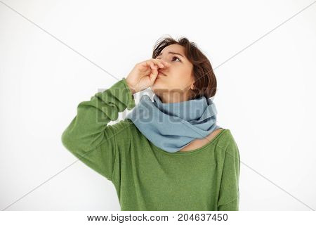Horizontal shot of worried unhappy young woman wrapped in scarf throwing head back having running nose while suffering from cold or flu. Sickness disease unwellness allergy and healthcare concept