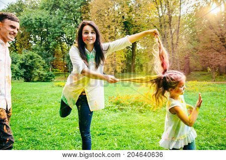father mother and daughter full around with holi paints in city park