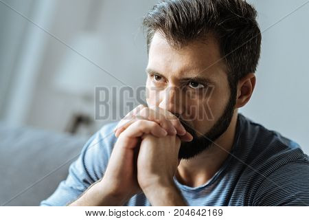 Absolute solitude. Cheerless thoughtful bearded man holding his chin and thinking about his life while feeling lonely
