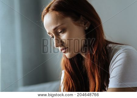 State of melancholy. Cheerless beautiful red haired woman being at home and feeling melancholic while having difficult times in life