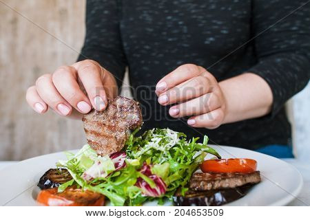Woman starts to eat medallions with salad. Grilled meat, tomatoes, eggplant and green ruccola with grated cheese, hunger and impatience, close up picture