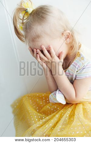 Weeping young blond girl indoor. Yellow dress