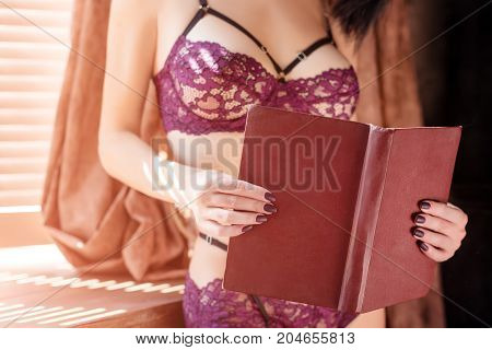 Sexy girl in fashion lace lingerie reading a book near the window