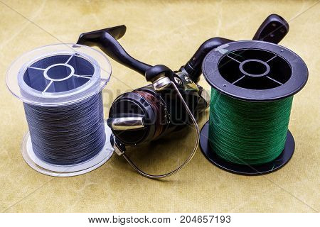 Fishing Reel And Spools Of Cords On The Background Of Tarpaulin. Green And Gray Fishing Line. Spools