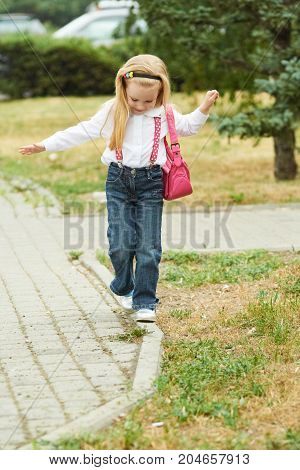 Young girl walk on curb. Jeans ping bag.