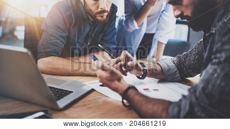 Teamwork concept.Group of three coworkers working together in modern coworking studio.Bearded man using smartphone and talk with partners about new startup project.Horizontal cropp.Blurred background