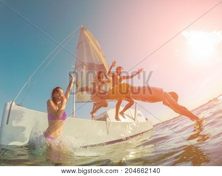 Happy friends diving from sailing boat into the sea - Young people jumping inside ocean in excursion day - Vacation youth and fun concept - Soft focus on right man head - Fisheye lens distortion