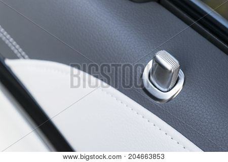 Door handle with lock contol buttons of a luxury passenger car. Black leather interior of the luxury modern car. Modern car interior details