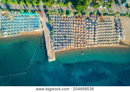 Aerial view of transparent turquoise sea, beautiful sandy beach with colorful chaise-lounges, boats, green trees, hotels, buildings at sunrise in Icmeler, Turkey. Summer seascape Top view from drone