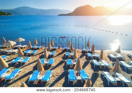 Aerial view of swimming woman on the air mattress in the sea against mountains at sunset. Summer seascape with girl, blue water and sandy beach with chaise-lounges. Top view. Travel in Icmeler, Turkey
