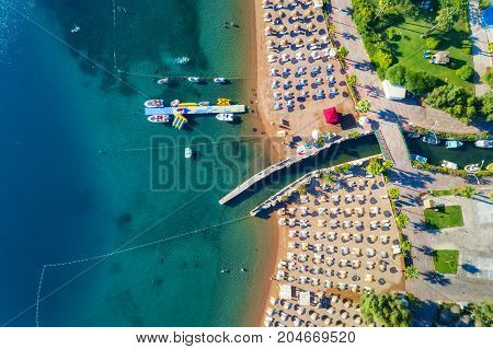 Aerial view of transparent turquoise sea, beautiful sandy beach with colorful chaise-lounges, boats, green trees, hotels, buildings at sunset in Icmeler, Turkey. Summer seascape Top view from drone