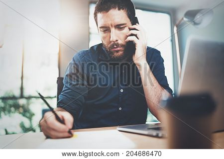 View of man hand making notes on paper document while sitting at the wooden table at sunny office.Blurred background. Horizonta
