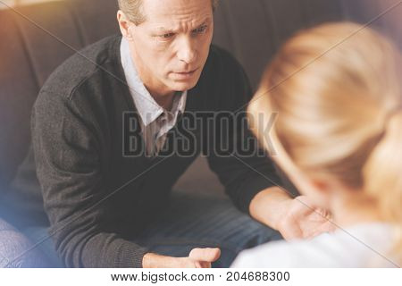 Psychological treatment. Cheerless nice adult man visiting a psychologist and asking her for advice while having personal problems