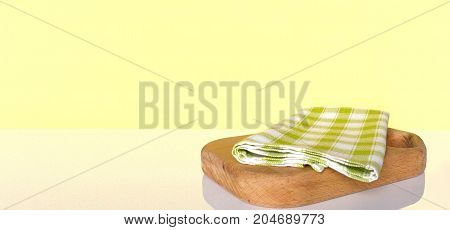 Cutting board with checkered green tablecloth on white table over yellow wall. Background with copy space