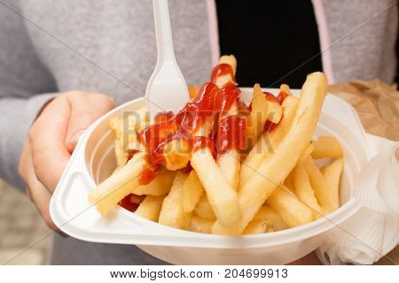 French fries with red sauce on a plastic plate closeup