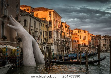Venice, Italy - May 20, 2017: Grand Canal with a pier for gondolas at sunset. Giant hands supporting the building are a sculpture by the artist Lorenzo Quinn.