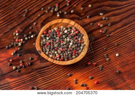 Peppercorns in a wooden bowl on a dark wooden background.